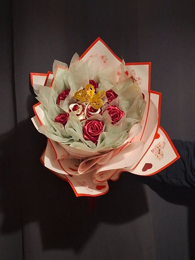 Bouquet de fleurs avec des roses rouges et des décorations dorées, entouré de feuilles.